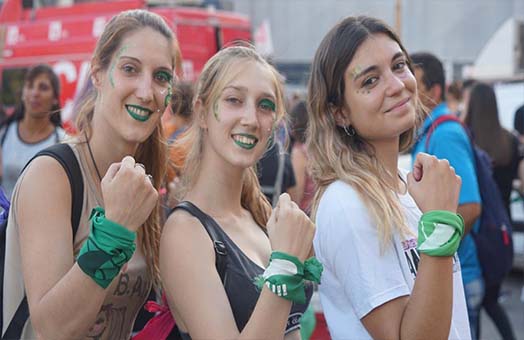 Tres chicas mirando la cámara con el pañuelo verde atado en sus muñecas