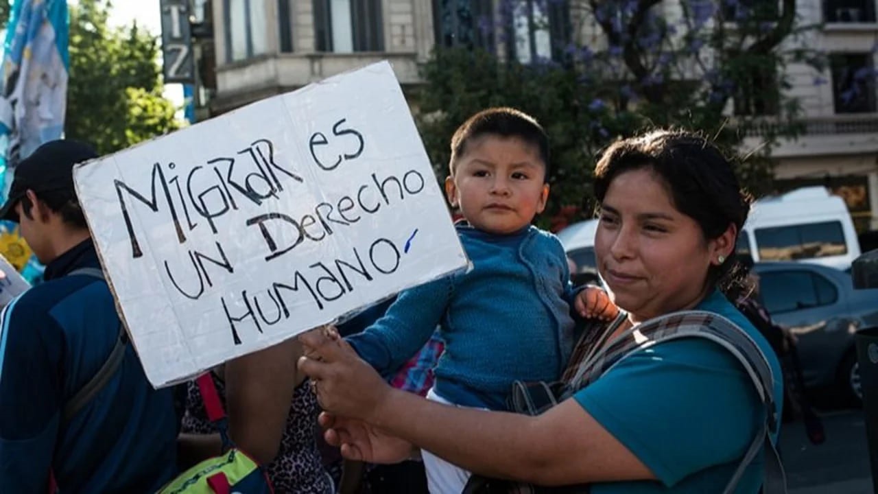 Mujer con nño en brazos con el cartel migrar es un derecho